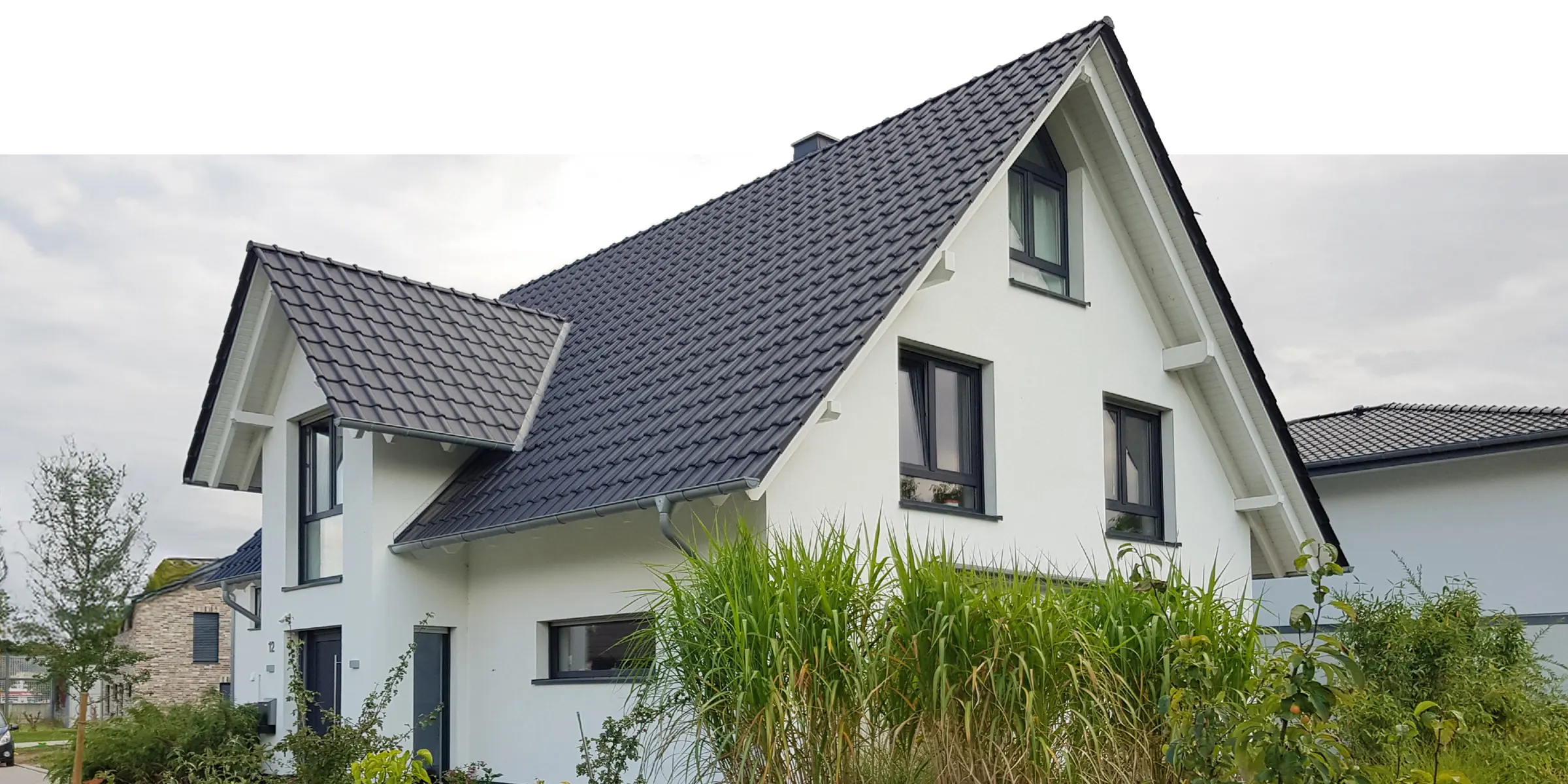 Weißes Einfamilienhaus mit dunklem Satteldach und Gräsergarten – gebaut von DENKER Eigenheim